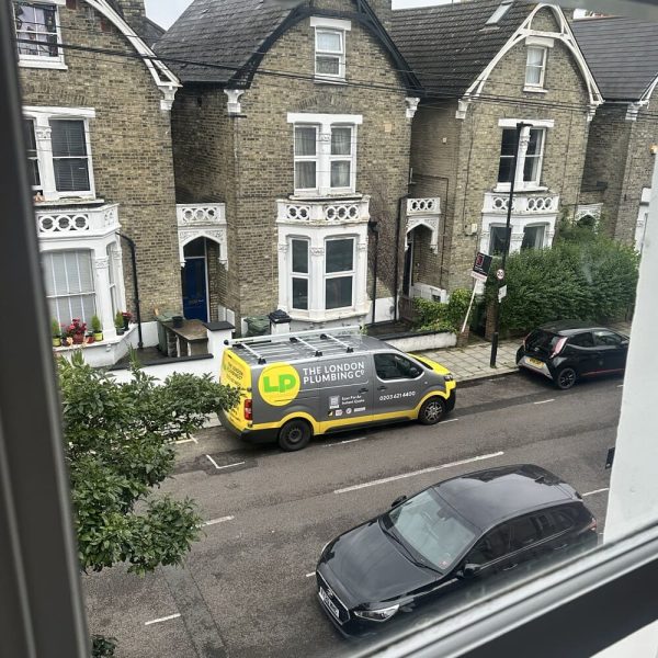 The London Plumbing Companys yellow, grey and green work van parked outside of houses on a road in Wimbledon.