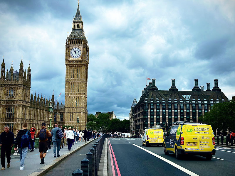 The London Plumbing Company yellow vans driving past Big Ben in London.