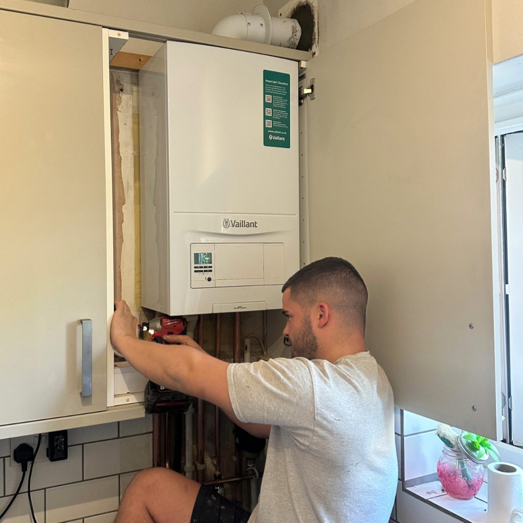 A 24-hour emergency London Plumbing Company engineer using a drill to help repair a boiler inside the kitchen cupboard of a flat in South London